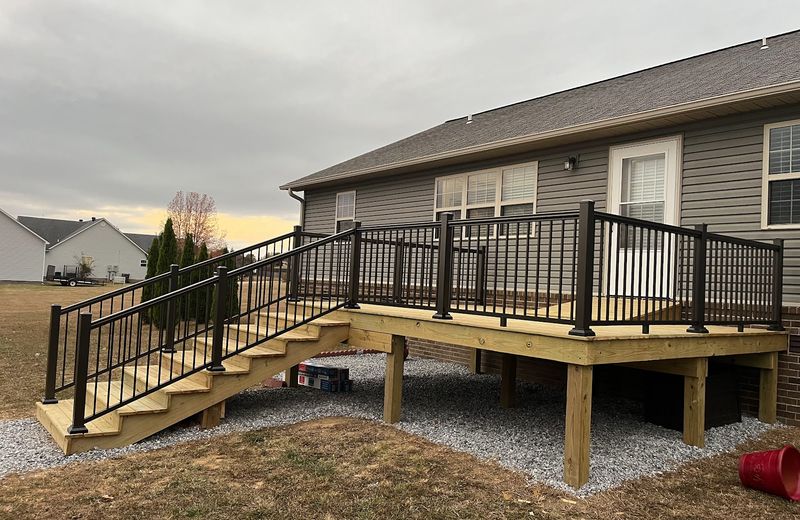 A deck built off the back of a ranch house with metal railing