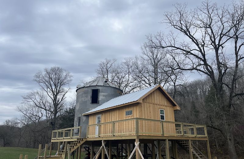 A house built on tall piers beside a repurposed grain bin
