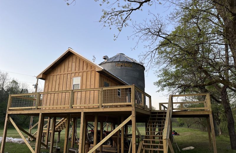 A grain-bin home on piers with a wraparound deck and stair